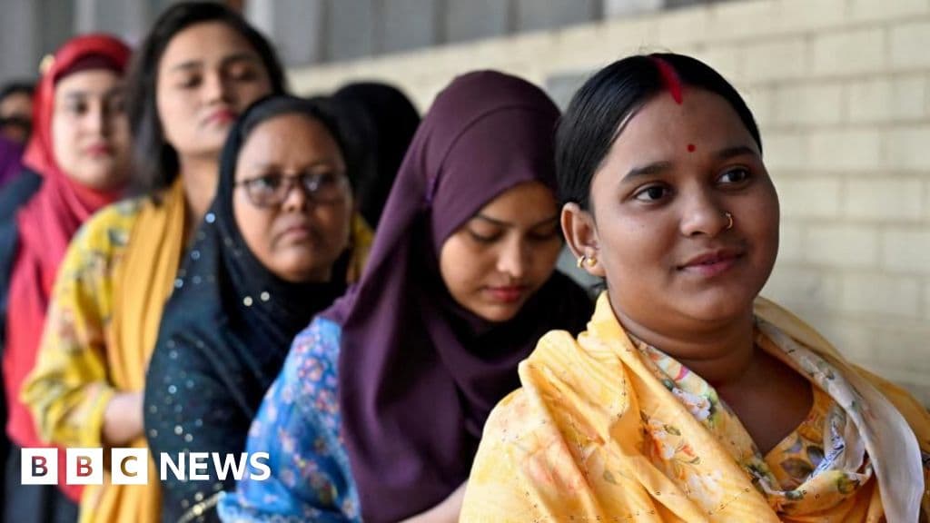 A gritty, realistic photo of a long line of exhausted voters in Dhaka, standing in the heat next to a concrete wall covered in torn and layered political posters, capturing a mix of hope and weariness.