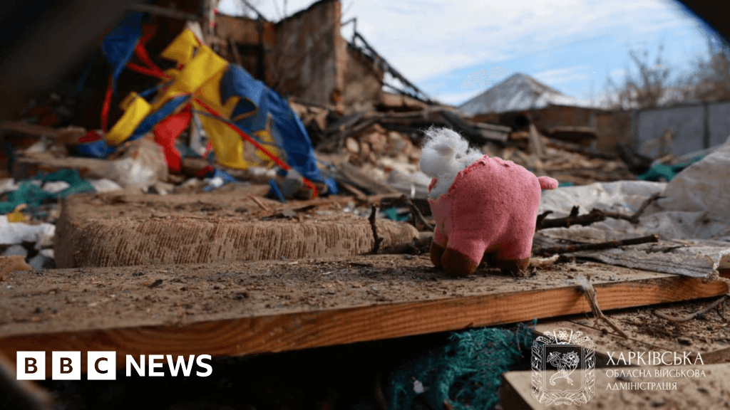 A gritty, high-contrast black and white photo of a single child's teddy bear lying abandoned in a pile of jagged concrete and brick rubble. Dust hangs in the air. The background is blurred ruins of a residential house. The mood is bleak, hopeless, and stark.