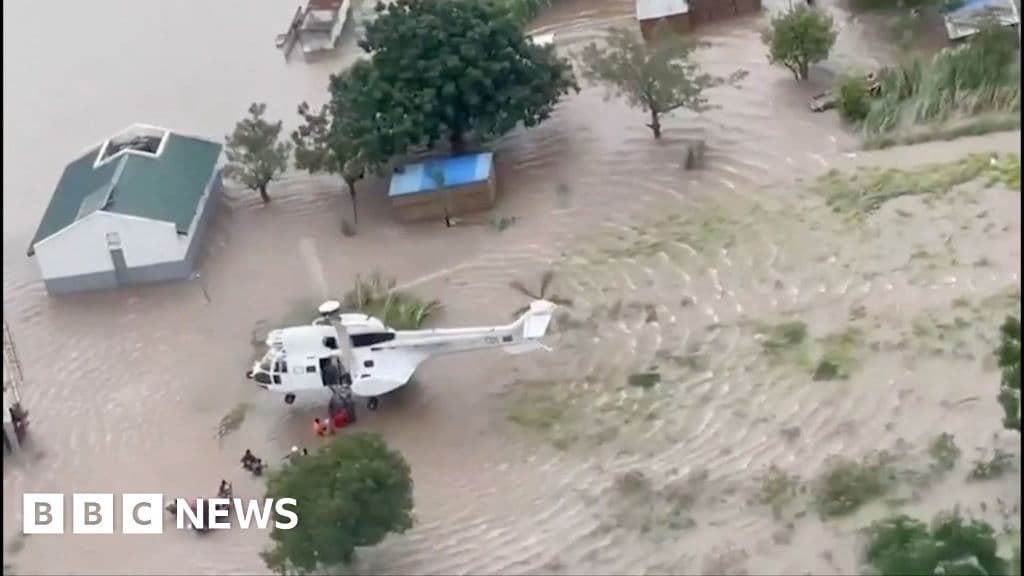 A hyper-realistic, gritty photojournalism style image of a vast, muddy flood landscape in Mozambique. The water is brown and murky, stretching to the horizon. In the foreground, the remains of a humble home, perhaps a thatched roof barely visible above the water line, and a single, brightly colored child's toy floating in the filth. The lighting should be overcast and gloomy, emphasizing the hopelessness and gray atmosphere. No people visible, just the devastating aftermath of nature.