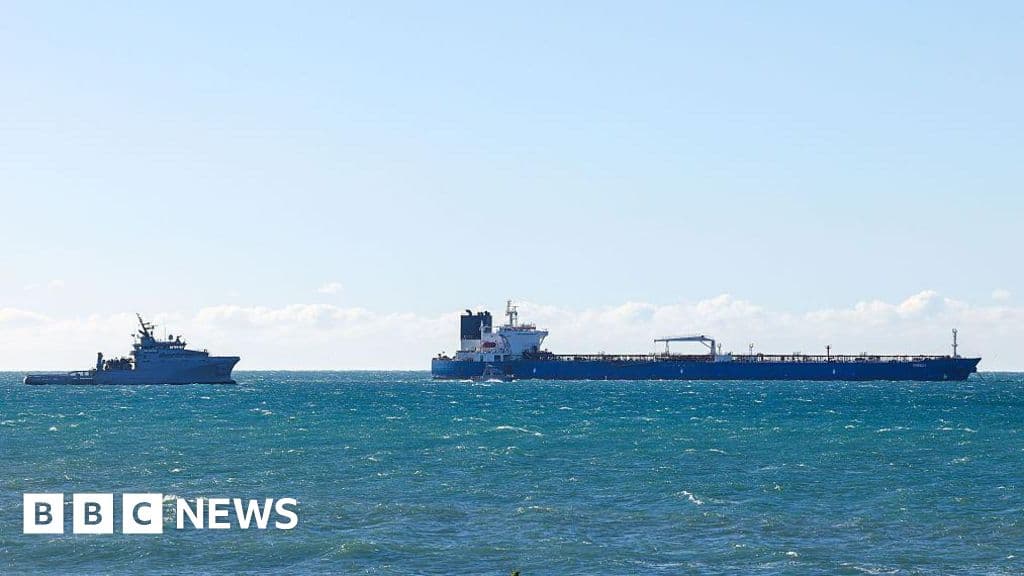 A gritty, realistic image of a large, rusty oil tanker sailing away from a beautiful French port at sunset. In the water behind the ship, instead of foam, there are floating euro banknotes swirling in the wake. The lighting is moody and cynical.