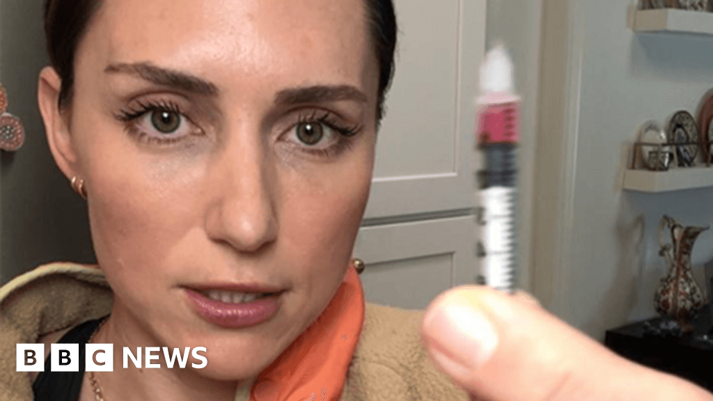 A gritty, slightly distorted photo of a generic fitness influencer holding a syringe filled with glowing neon green liquid, smiling blankly, standing in a messy kitchen that looks like a makeshift laboratory.