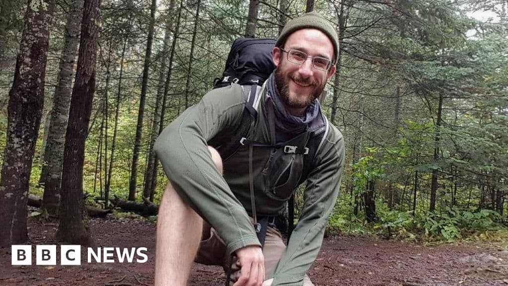 A gritty, desaturated photo of a large stack of legal paperwork sitting on a cold metal desk, with the blurred red and blue lights of a police car reflecting through a window in the background.