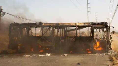 A conceptual editorial illustration of a heavy golden crown lying broken in the mud, surrounded by dirty military boot prints. The lighting is dark and moody, with a cynical and gritty atmosphere. No text.
