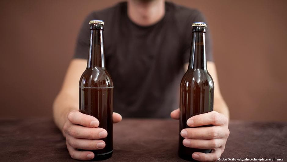 A hyper-realistic, cynical depiction of a traditional German beer hall that is completely empty and sterile. On a wooden table sits a single, half-empty glass of water and a pile of complex, daunting tax forms with a German government seal. Through the window, the grey, overcast sky of Berlin looms over a landscape of construction cranes and bureaucratic buildings. The lighting is cold and clinical, highlighting the dust on the abandoned beer taps. High contrast, sharp details, satirical and bleak atmosphere.