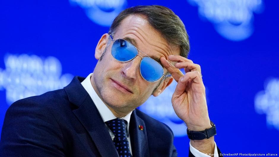 A satirical oil painting in the style of a chaotic Baroque masterpiece. In the center, a miniature Emmanuel Macron stands on a pedestal made of leather-bound books, pointing a tiny silver sword at a giant, golden-haired Donald Trump who is trying to put a 'SOLD' sign on a melting iceberg labeled 'Greenland'. In the background, the Eiffel Tower is made of gold coins and the Statue of Liberty is wearing a beret. The atmosphere is smoky and absurd, with dark, dramatic lighting and a sense of impending doom.