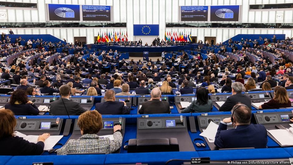 A hyper-realistic, satirical digital painting of the European Parliament building appearing as a crumbling, ancient ruin made of stacks of dusty legal documents. In the foreground, a group of politicians in expensive, identical grey suits are frantically burying a giant, glowing scroll labeled 'MERCOSUR' in a shallow grave made of red tape. The lighting is cold and bureaucratic.