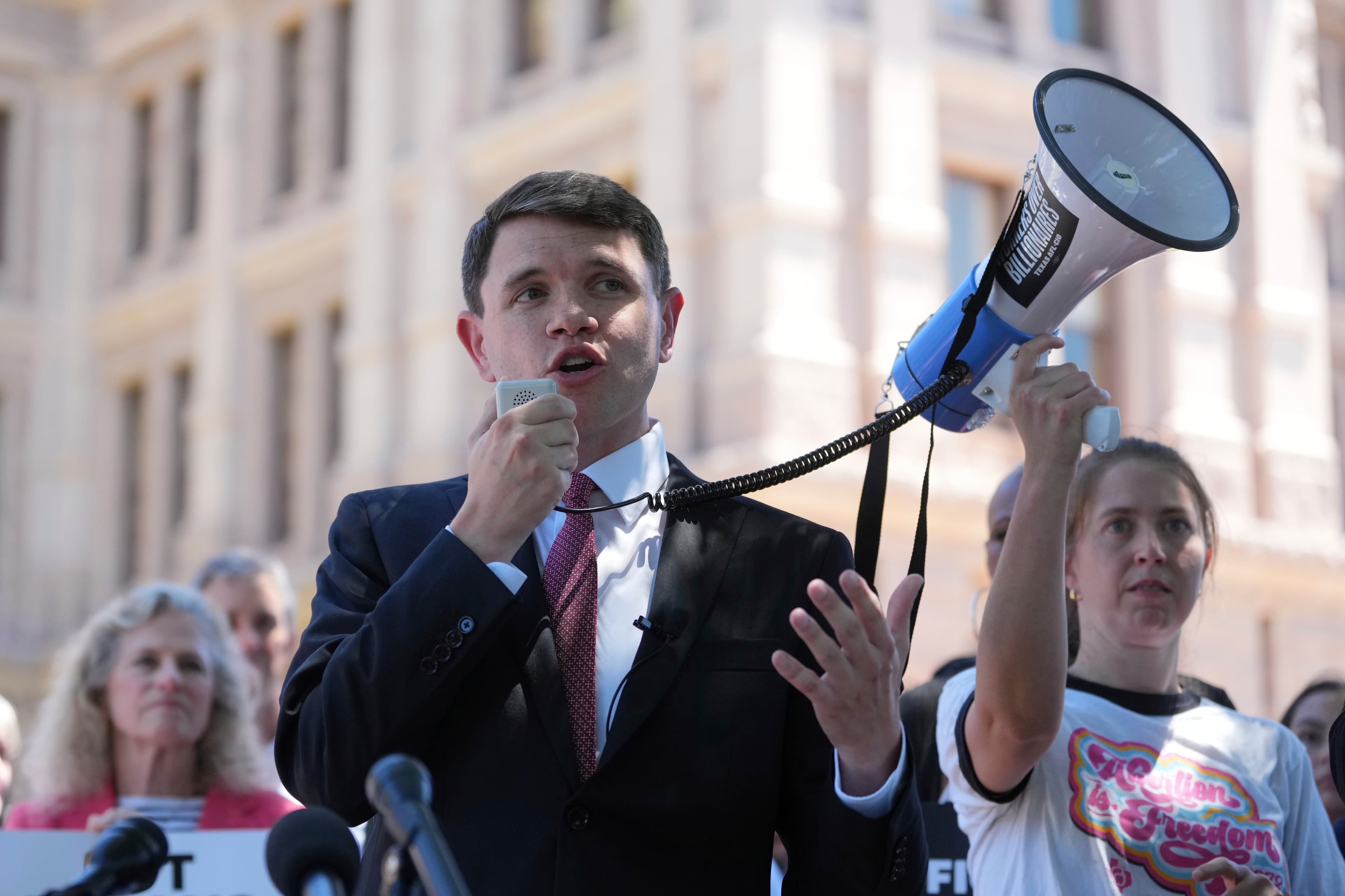 A gritty, satirical illustration of the Texas State Capitol building sinking into a desert of quicksand made of shredded ballots and dollar bills. In the foreground, two figures representing a generic Democrat and a generic Republican are fighting over a megaphone while standing on a sinking pedestal. The style is dark, acid-toned, and reminiscent of a 1970s political caricature.