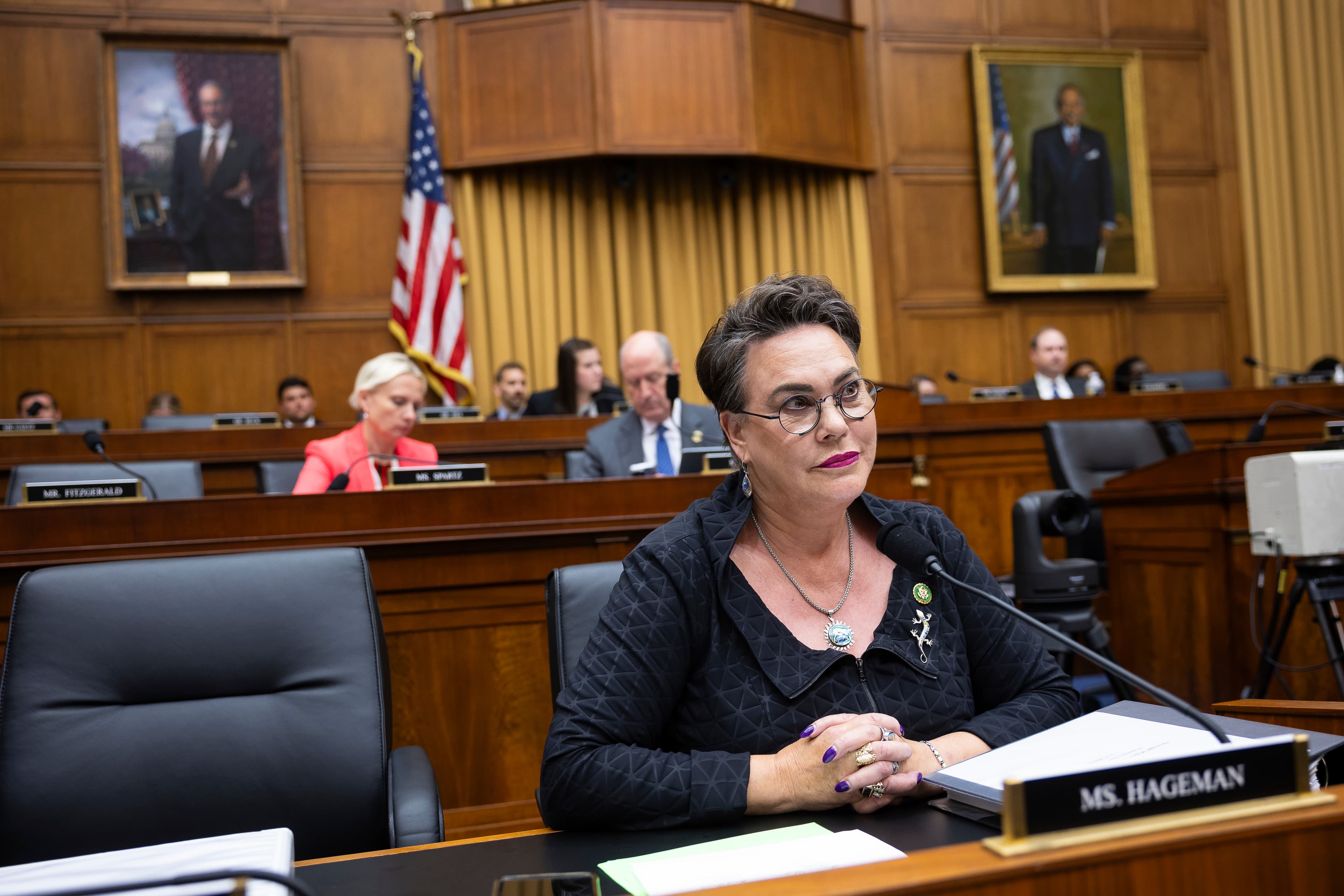A satirical oil painting of Harriet Hageman dressed in Roman senatorial robes but with a MAGA red trim, standing in a desolate Wyoming desert. In the background, the U.S. Capitol building is sinking into a giant hole shaped like a ballot box. The lighting is dramatic and gloomy, capturing a sense of cynical political theater.
