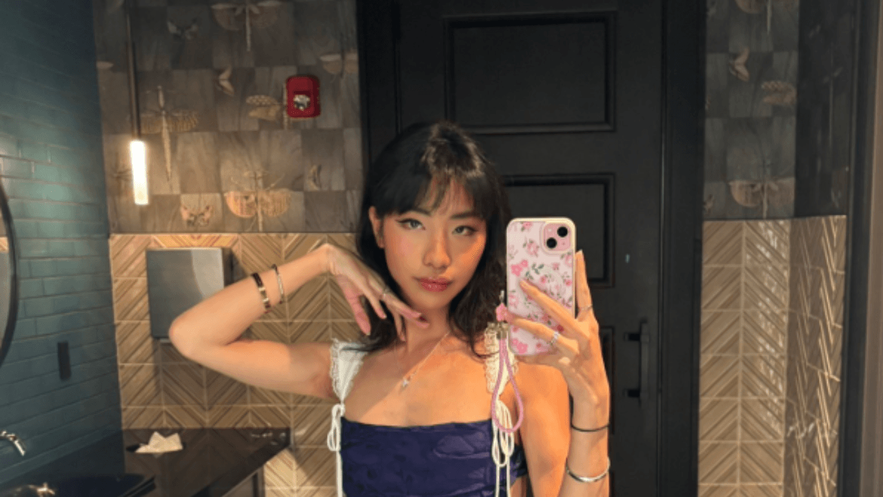 A cynical, dark-haired man in a suit sitting in a dimly lit office with a neon Marvel Rivals sign flickering in the background, looking with intense boredom and disdain at a computer monitor showing a chaotic, colorful superhero video game. The man is holding a glass of scotch and there is a stack of philosophy books gathering dust on his desk.