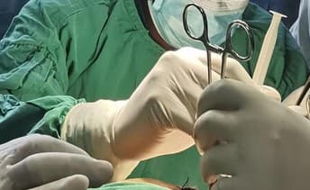 A satirical, high-contrast digital illustration in the style of a vintage European political cartoon. A spotlight with the UN and EU logos beams down onto a single, ornate, old-fashioned sewing machine sitting in the middle of a barren Malawian landscape. The shadow cast by the sewing machine is in the shape of a medical surgical lamp. In the background, a group of faceless bureaucrats in grey suits are applauding, holding a banner that reads 'Dignity Project: Batch #400'. The sky is a cynical shade of bruised purple and grey.