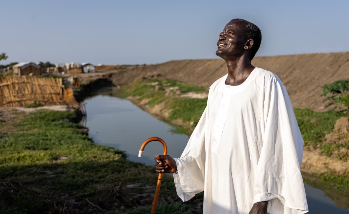 A satirical editorial cartoon style illustration. In the center, a golden, locked ballot box sits atop a mountain of bureaucratic paperwork and unfulfilled peace treaties. Two men in expensive suits and military hats are leisurely painting '2026' over a faded '2022' date on a sign that says 'Elections'. In the background, international diplomats are looking through binoculars from a luxury tent, holding a banner that says 'Success!'. Gritty, high-contrast, acidic colors.