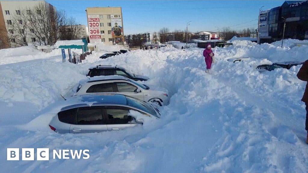 A desolate street in a Russian city completely buried in deep snow. Several cars are just vague mounds under the white powder. A single person in a thick coat holds a shovel, looking small and defeated against the massive snowdrifts. Grey, overcast sky. high contrast, gritty realism.