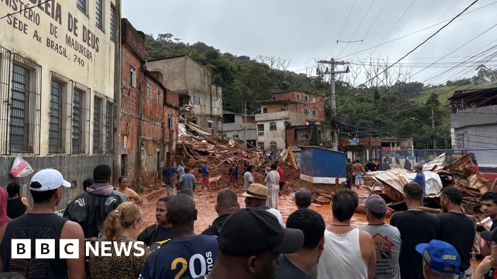 A moody, high-contrast photojournalistic image of a rain-soaked Brazilian hillside slum in the aftermath of a landslide. The scene is dominated by brown mud and debris. In the foreground, a single, brightly colored child's toy is half-buried in the sludge, highlighting the tragedy. In the background, rescue workers in orange vests are blurred, working near a collapsed structure. The sky is grey and oppressive. No recognizable faces.