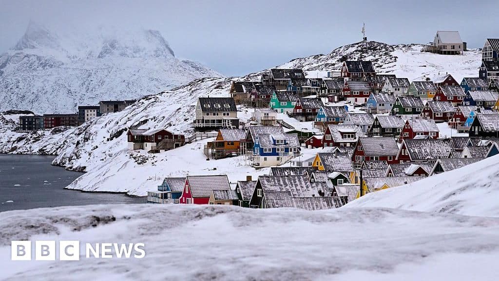 A photo of the colorful houses of Nuuk, Greenland, sitting on rocky terrain with snow, under a grey, overcast sky, representing a remote and strategic location.