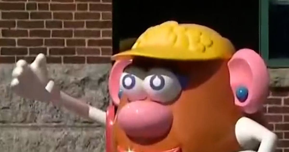 A close-up, gritty, and slightly desaturated photo of a dirty car bumper in Rhode Island. The license plate is rusted and features a faded, peeling image of Mr. Potato Head. The car is stuck in traffic under a grey, overcast sky. Raindrops are on the lens.