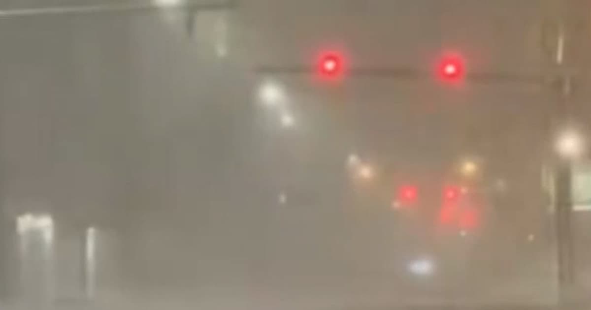 A hyper-realistic, gloomy image of a frozen American suburban street. A power line is sparking and snapping in half under the weight of ice. In the foreground, a grocery bag spills milk onto the snow. In the background, a billboard shows a smiling politician with the text 'STAY WARM' while the city behind it is dark.