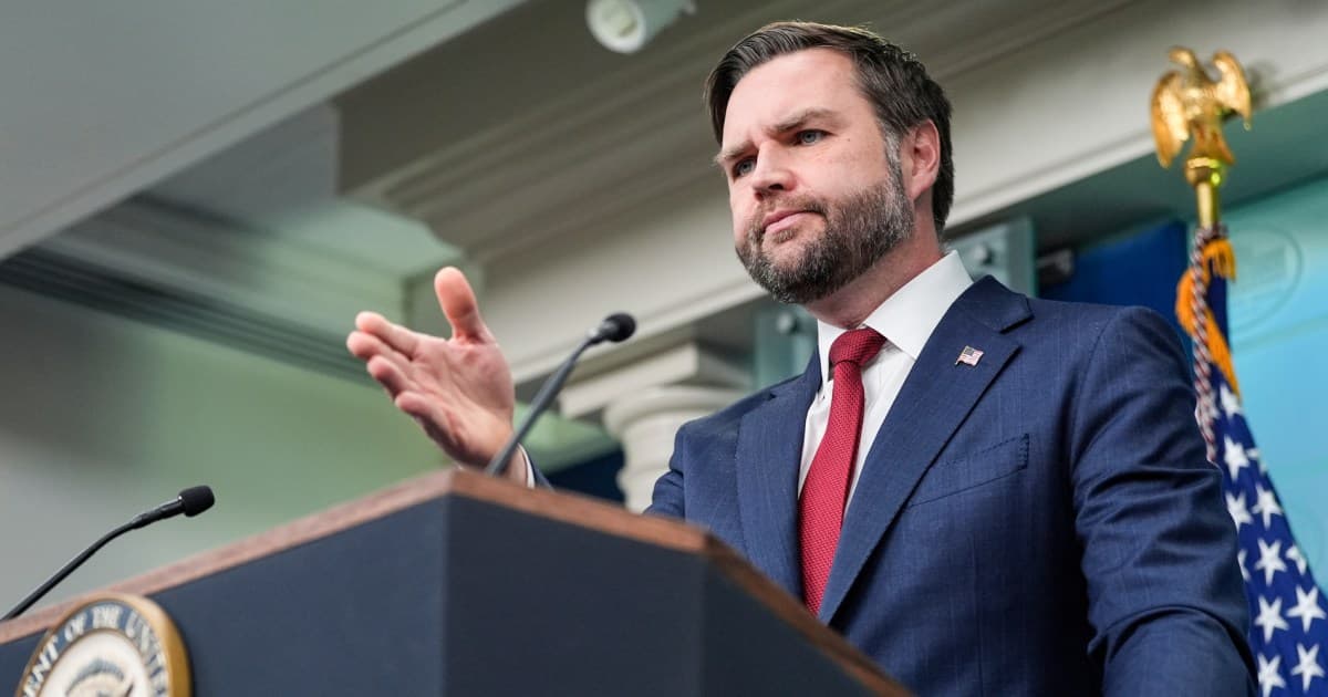 A satirical illustration of a politician resembling JD Vance standing in the middle of a snowy Minneapolis street. He is holding a fire hose, but instead of water, it is spraying bright red gasoline onto a smoldering fire. He is wearing a suit with a 'PEACEMAKER' sash. In the background, rival groups of caricatured protesters and ineffective city officials are yelling at each other, ignoring the fire. The sky is grey and oppressive.