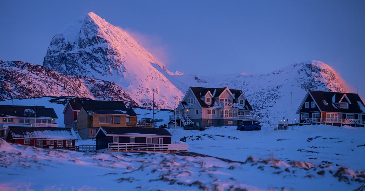A surreal, cynical satirical illustration in a muted, cold color palette. In the foreground, a golden, tacky 'SOLD' sign is being hammered into a vast, icy glacier landscape representing Greenland. In the background, the Davos Swiss Alps are visible, where silhouetted figures in suits sip champagne, indifferent to the transaction. The atmosphere is cold, bureaucratic, and absurd, blending 19th-century imperialism with modern corporate sterility.