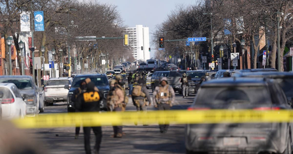 A gritty, low-angle view of a shattered smartphone lying on wet asphalt, reflecting the flashing red and blue lights of police cruisers. The screen is cracked but glowing, showing a blurry frozen frame of a chaotic street scene. The background is dark and out of focus, filled with the silhouettes of federal agents and yellow caution tape. The atmosphere is cold, cynical, and noir-like.