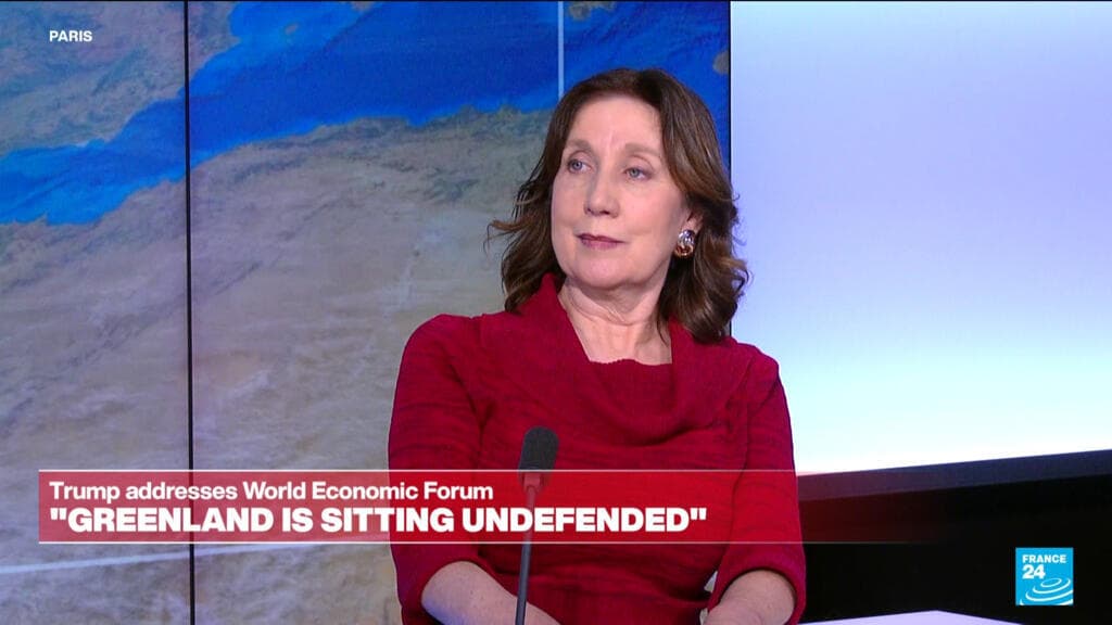 A wide-angle, cynical painting of the Davos conference hall. In the center, a distorted, towering figure of Donald Trump stands at a podium made of gold-plated bricks, gesturing wildly at a giant wall map where Greenland is being covered by a 'SOLD' sticker. The audience consists of faceless, tuxedo-clad figures with champagne flutes, sitting in rows made of stacks of burning dollar bills. The lighting is cold and clinical, reflecting off the snowy peaks of the Swiss Alps visible through the windows. The style is sharp, satirical, and slightly surrealist, emphasizing the absurdity of the scene.