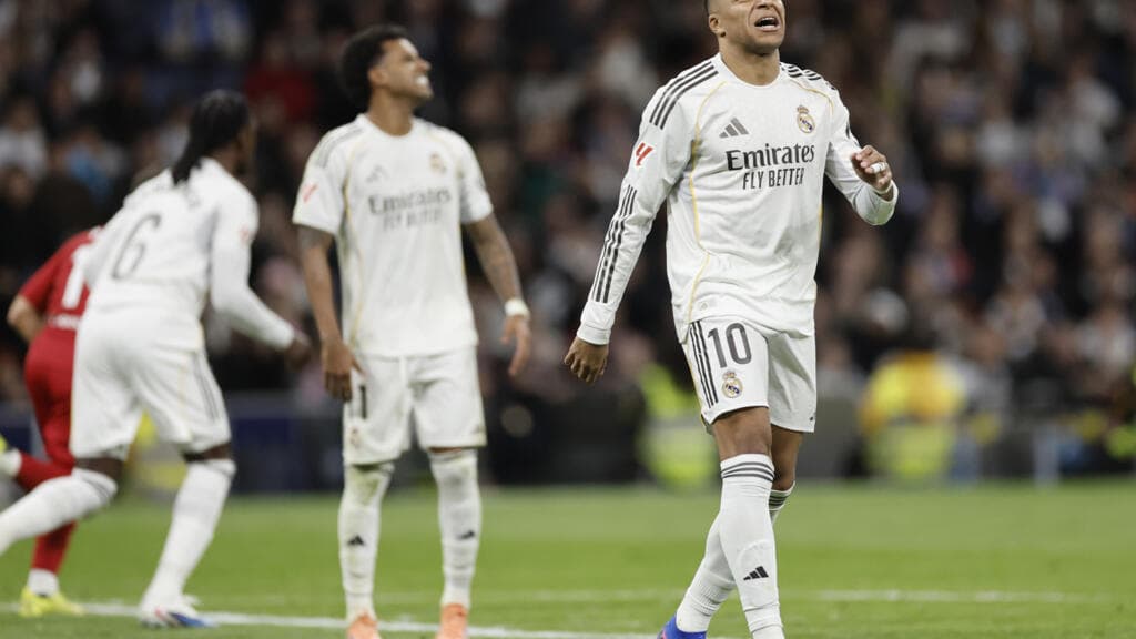 A cynical, dark satirical illustration of a giant, golden Real Madrid logo shaped like a steamroller, crushing a small, fragile glass bottle labeled 'Monaco' on a football pitch. Kylian Mbappe stands in the background, looking bored and checking a golden watch, while Alvaro Arbeloa stands on the steamroller wearing a crown made of money. The stadium is filled with shadowy, faceless fans holding white handkerchiefs. High contrast, sharp, acidic colors.
