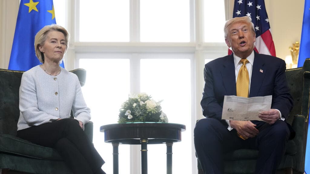 A satirical, high-contrast digital painting of a massive gold-plated 'TRUMP' sign being airlifted by helicopters toward a snowy, majestic Greenland landscape. In the foreground, a group of frantic, grey-faced European bureaucrats are trying to stop the helicopters with long, tangled strands of red tape and oversized rubber stamps. The sky is a stormy, cynical grey, and the ocean is filled with floating trade documents. Detailed, biting caricature style.