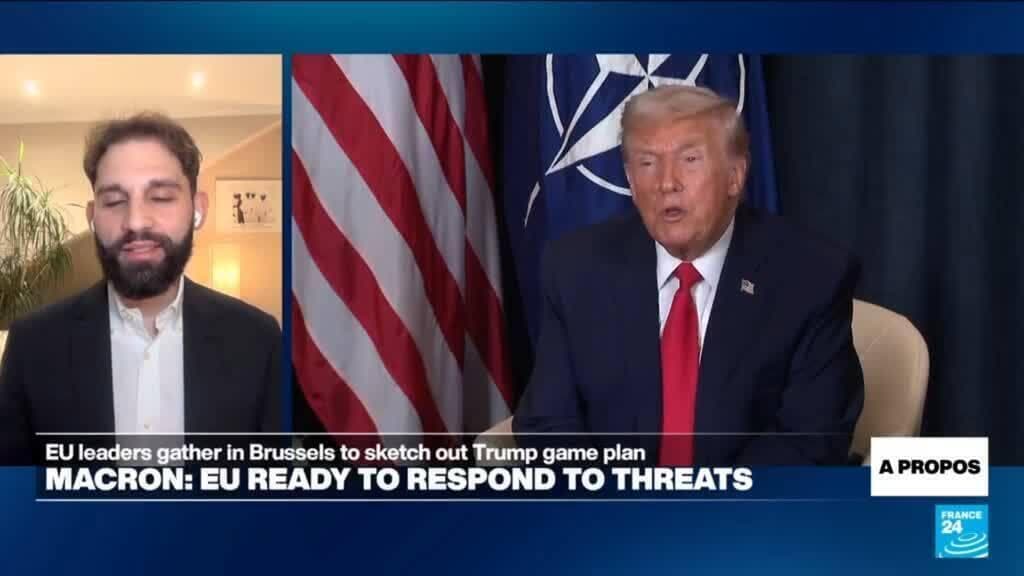 A group of stiff European politicians in suits, all wearing oversized, ill-fitting blonde wigs and trying to look tough, while a giant golden statue of a businessman looms in the background and a crowd of bored people walks away.