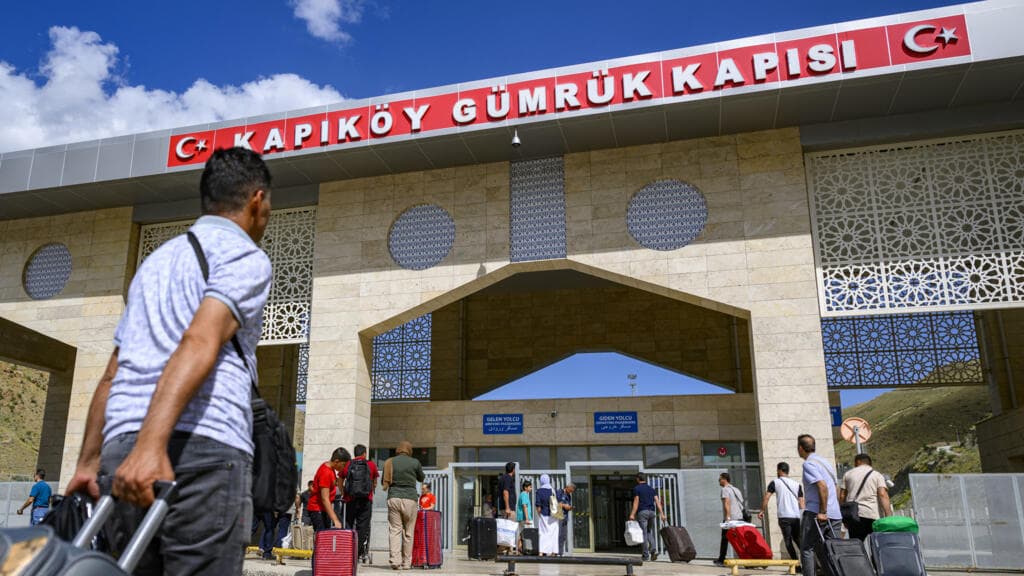 A dark, satirical oil painting of a Turkish and Iranian official shaking hands over a map that is cracking and bleeding, with the shadow of a riot policeman looming over them in a smoky, dark hallway.