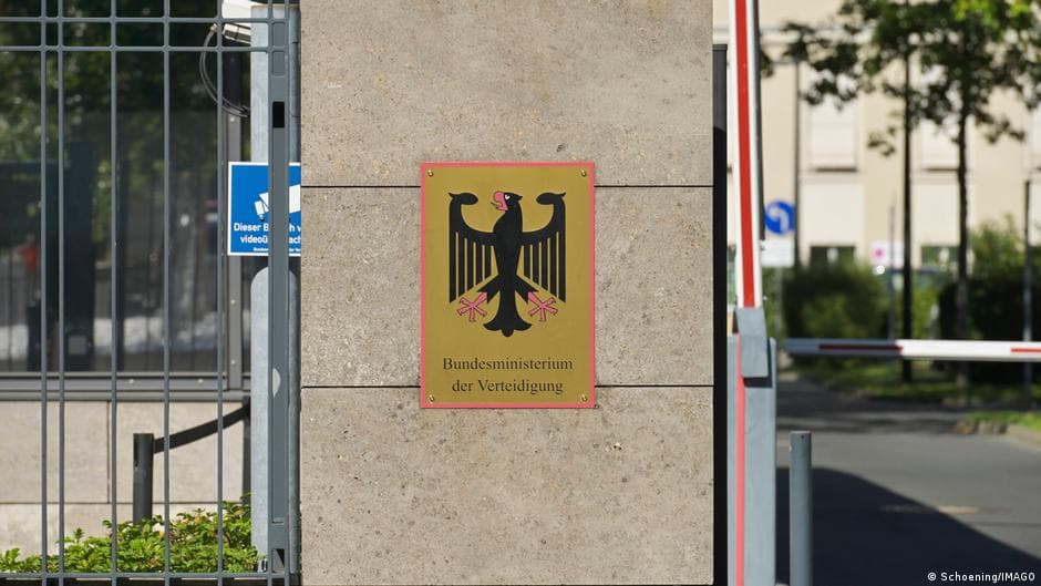 A satirical, dark oil painting of a bleak, rainy Berlin street. In the foreground, a woman with a dual-flag lapel (German and Ukrainian) hands a dull grey USB drive to a shadowy figure in a polyester suit standing in front of the Russian Embassy. In the background, a group of Germans look on with expressions of profound, sober misery, holding empty beer mugs. The sky is a bureaucratic grey, and the Brandenburg Gate is crumbling slightly in the distance. Low saturation, gritty textures.