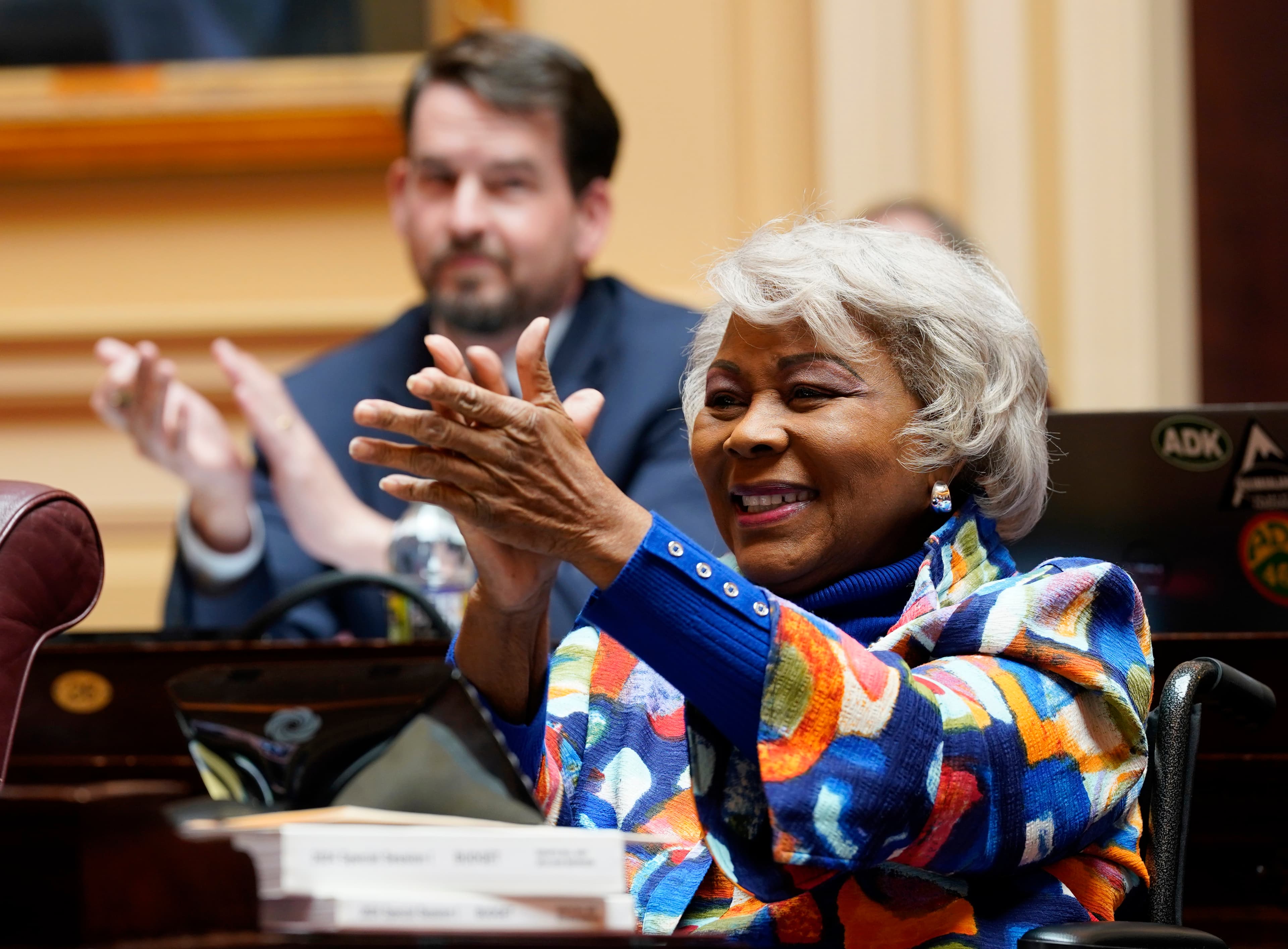 A cynical, high-contrast illustration of two shadowy, faceless figures in suits (one with a blue tie, one with red) fighting over a map of Virginia. The map is being torn apart and redrawn with jagged, glowing neon lines. In the background, an old-fashioned printing press is being crushed by a giant, soulless computer server. The lighting is cold and oppressive, capturing a feeling of bureaucratic dread.