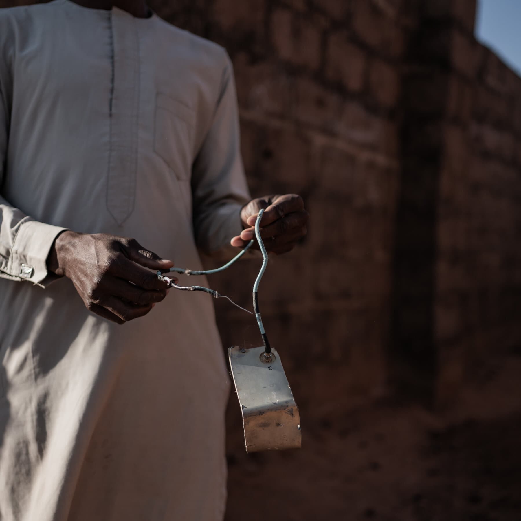 A gritty, high-contrast illustration of a fat man in a suit wearing an American flag pin, eating a steak dinner at a fancy table. The table is set on top of a map of Africa. In the background, blurry smoke rises. The style is dark, cynical, political cartoon realism.