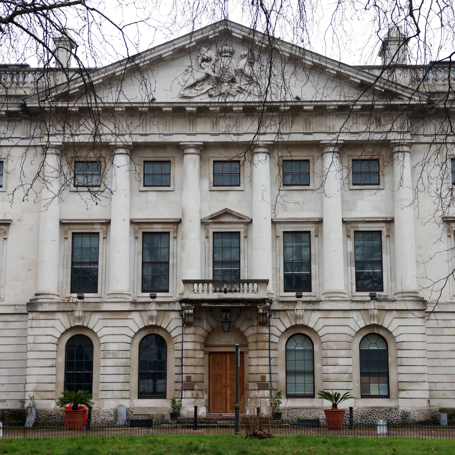 A photorealistic, slightly grainy news photo of the London skyline near Tower Bridge. In the foreground, a menacing, ultra-modern brutalist building is under construction. The building features an comically oversized, cartoonishly large telescope sticking out of the side, clearly aimed at the Palace of Westminster in the distance. The roof is covered in hundreds of aggressive-looking satellite dishes and radar arrays. A British flag limply hangs next to a massive surveillance camera.