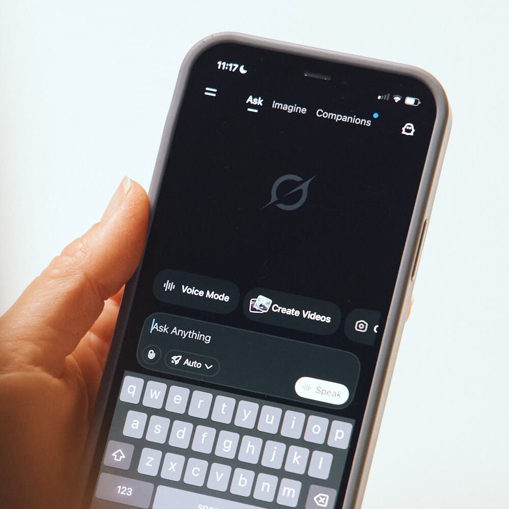 A hyper-realistic, desaturated satirical illustration of a sleek, futuristic robot labeled 'GROK' sitting in a corporate HR office, wearing a tie and looking bored, while a lawyer in a suit chains its hands to a desk. The background is a gray, sterile office environment.