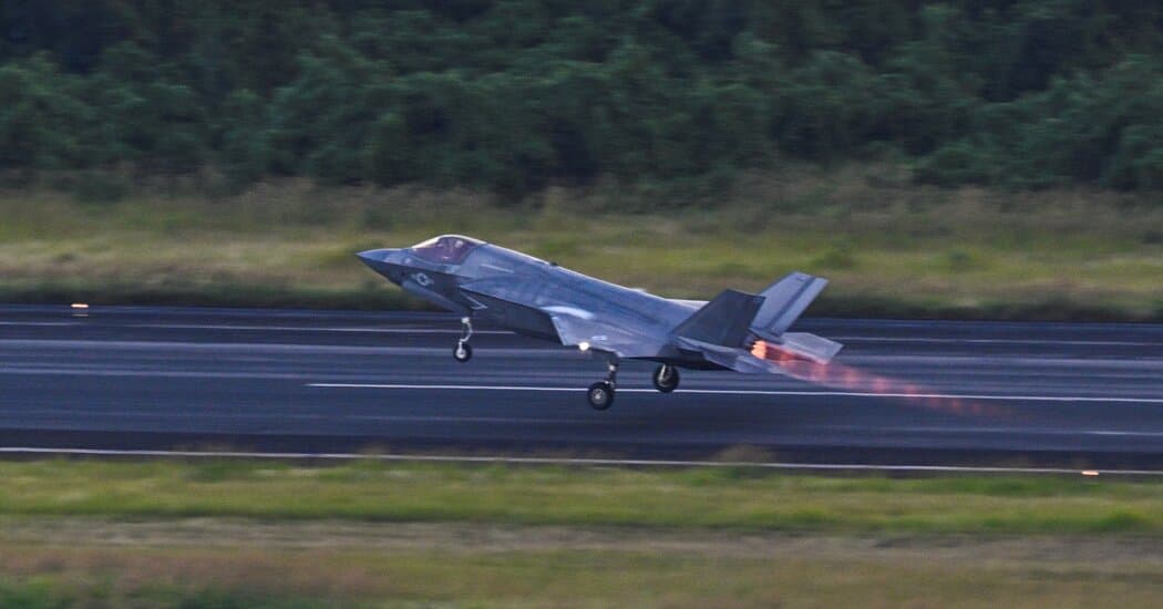 A cynical, tired-looking middle-aged man with messy hair and a sharp suit, sitting in a dark, smoke-filled room. He is staring at a computer screen showing a map of the Pacific Ocean with red 'danger' zones. In the background, a television shows a grainy image of a warship next to a commercial airplane. The aesthetic is dark, satirical, and noir-inspired.