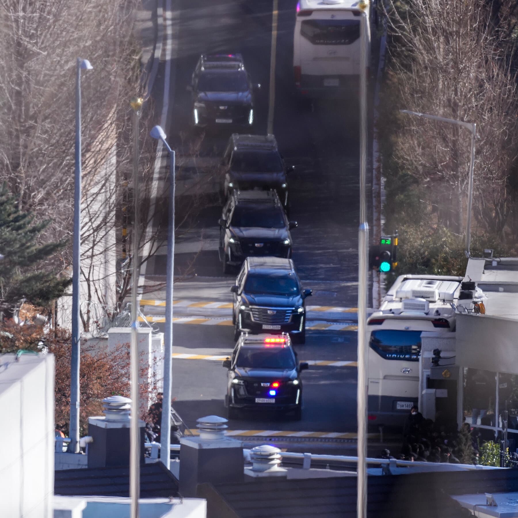 A photorealistic news image of former South Korean President Yoon Suk Yeol standing in a courtroom looking sheepish and shrugging his shoulders while a judge glares at him over reading glasses.