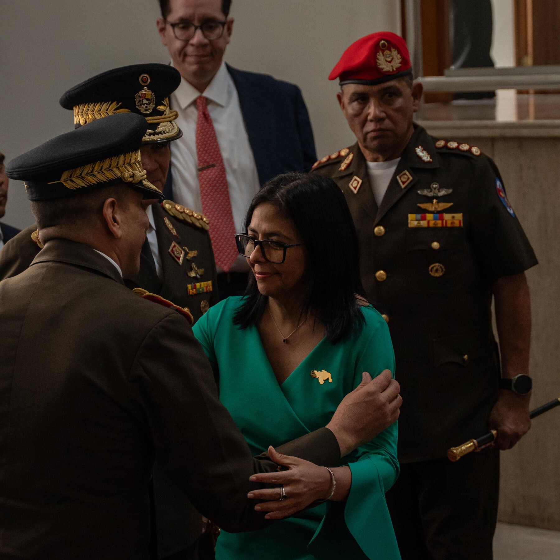 Donald Trump standing at a podium in the Rose Garden, looking frustrated and confused as he tries to insert a gasoline pump nozzle into a cardboard voting box labeled 'VENEZUELA'.