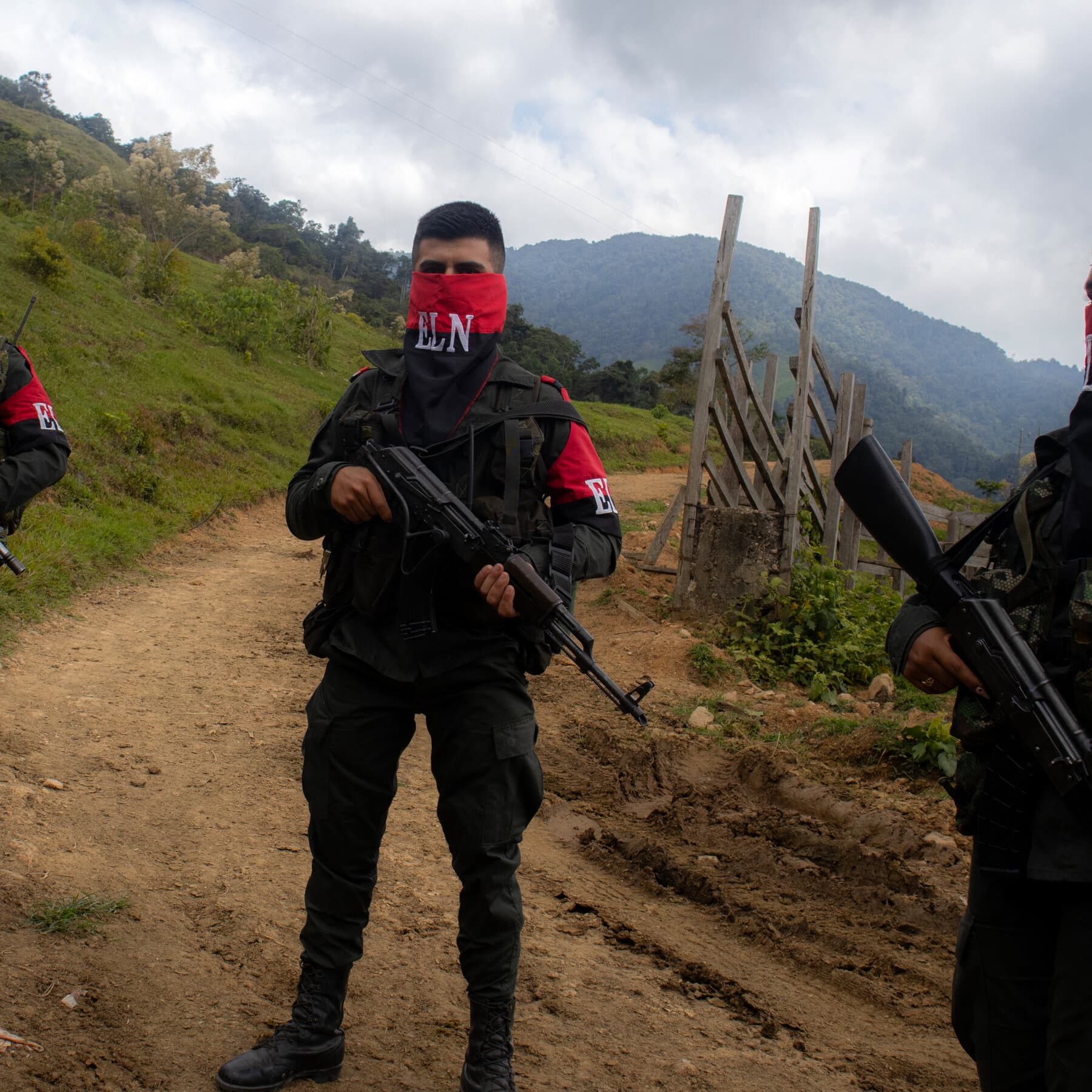 A satirical news photo of Colombian President Gustavo Petro sitting at his desk holding a phone receiver. He is wearing dark aviator sunglasses and a red tie that is slightly too long. He looks manic and is giving a thumbs-up while pointing to a map of the jungle marked with big red 'X's. In the background, a portrait of Simon Bolivar has been hastily covered with a poster of a steak.