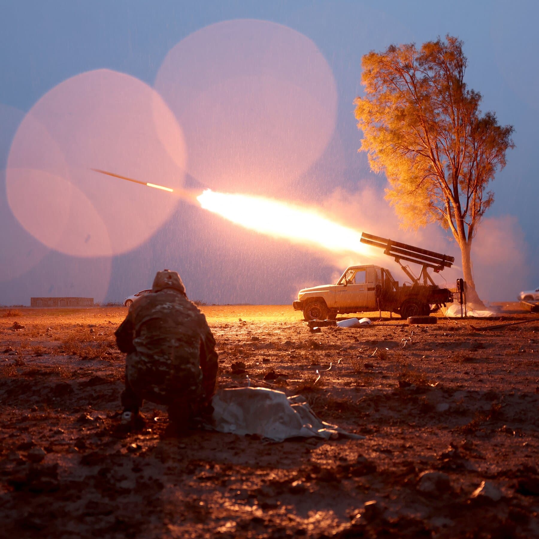 A photorealistic news image of a Syrian T-72 tank rolling through a dusty conflict zone, but the tank barrel has a giant sound suppressor silencer attached to the end of it, and the soldiers are wearing librarian cardigans.