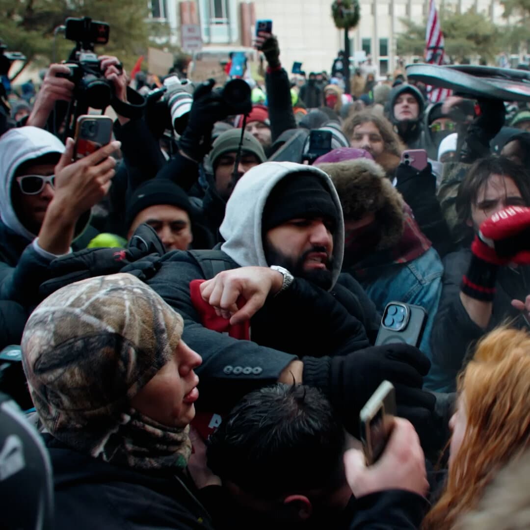A gritty, high-contrast, black-and-white illustration of two identical, faceless figures punching each other in a mirrored reflection. The background is a blurred, gray cityscape of Minneapolis under a heavy, oppressive sky. The style should be reminiscent of political cartoons but darker and more nihilistic.