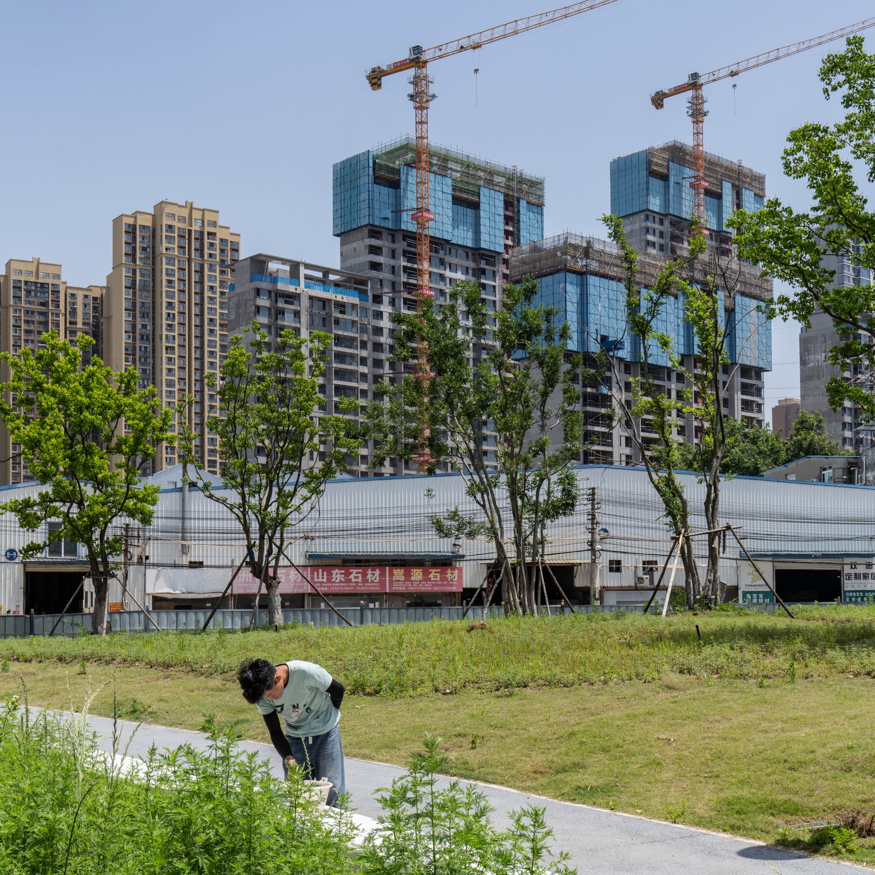 A hyper-realistic, desaturated image of a crumbling, unfinished Chinese skyscraper made of grey concrete. The debris falling from the building turns into shipping containers as it hits the ground. In the foreground, a singular, pristine red percentage sign '%' stands amidst the rubble.