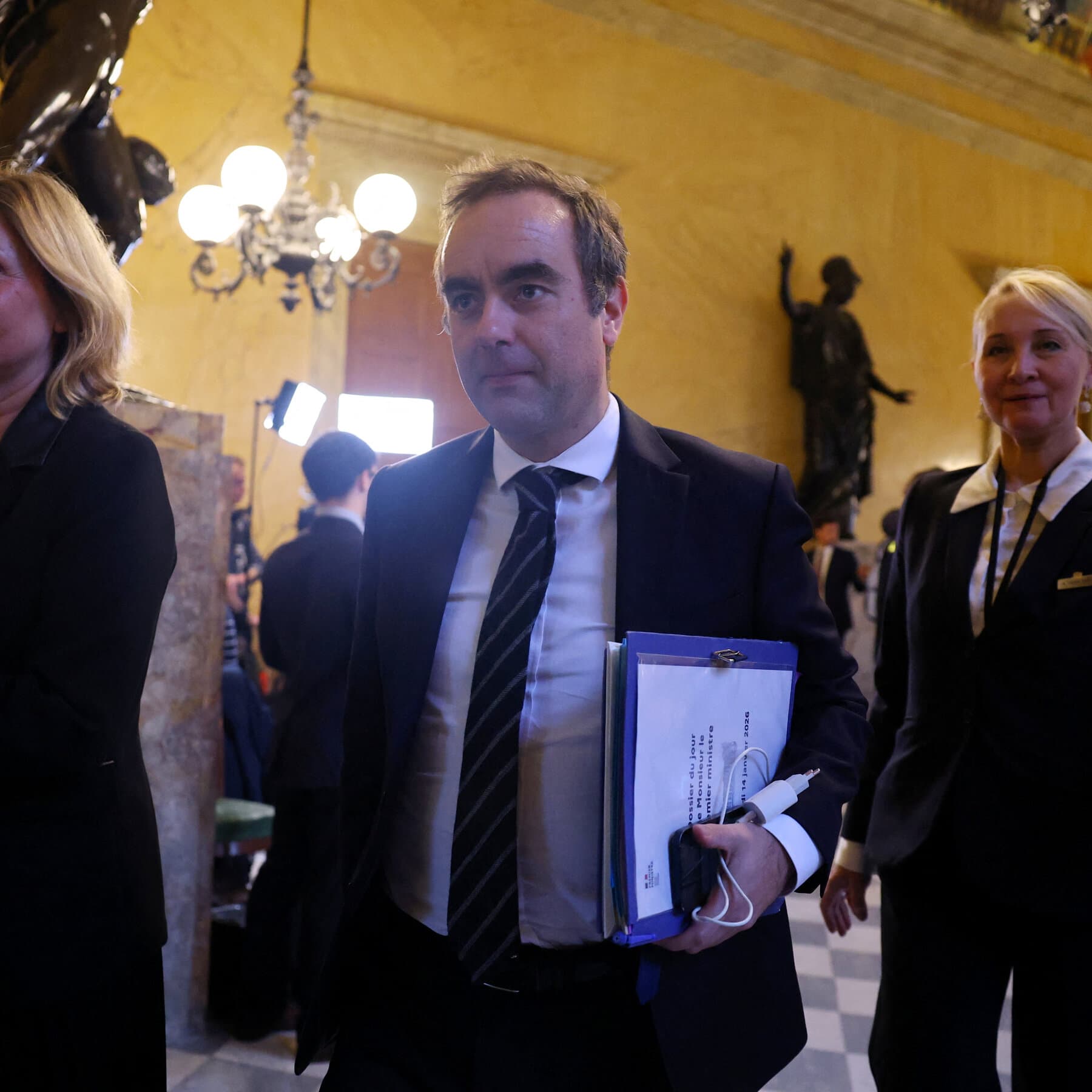 A photo of French Prime Minister Sébastien Lecornu standing at a podium in the French National Assembly looking bored and checking his wristwatch, while in the blurry background, furious politicians are throwing stacks of paper into the air and screaming.