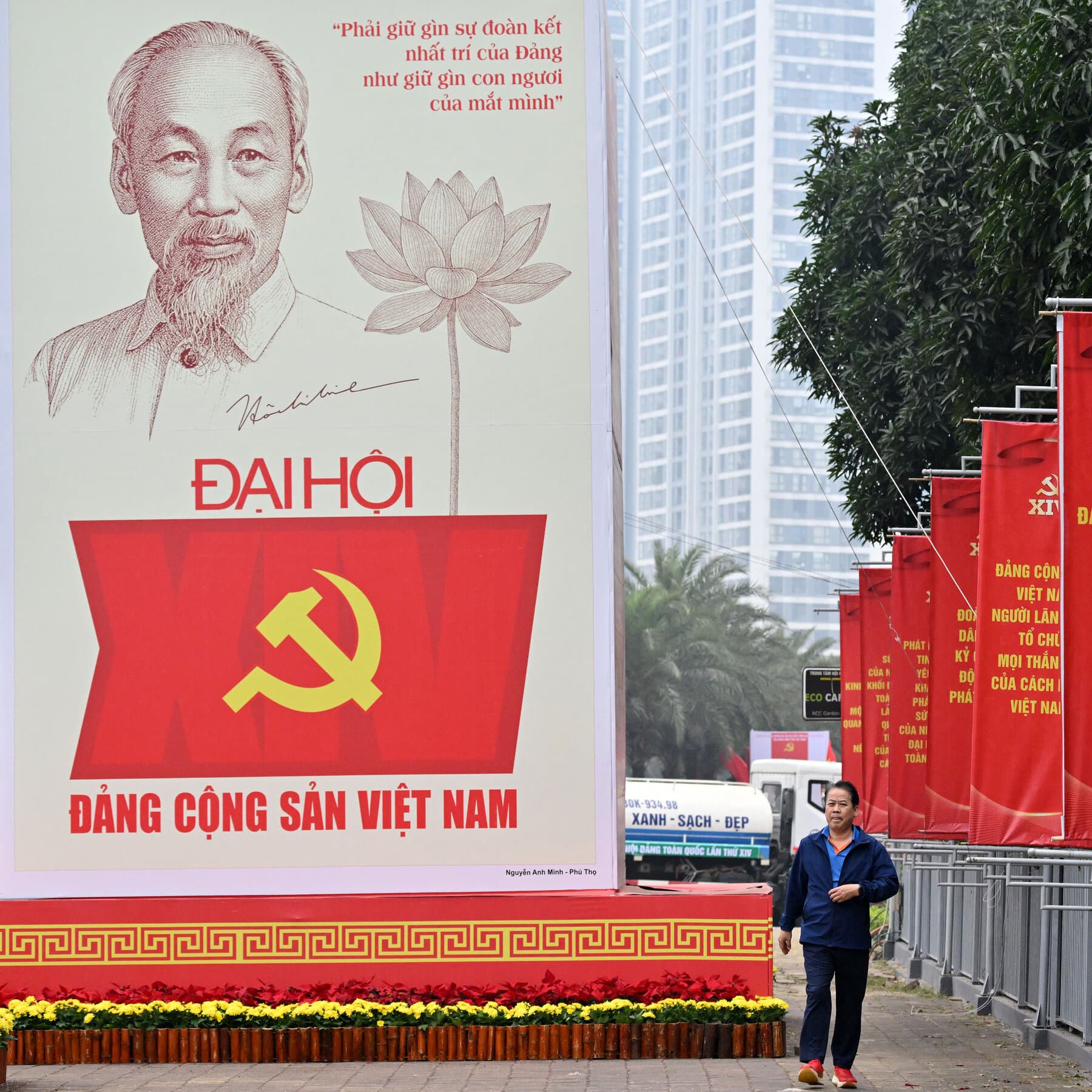 A hyper-realistic, dark satirical painting of an ancient, stone-faced communist official in a drab suit, sitting at a mahogany desk. On the desk is a golden bust of Ho Chi Minh, but the bust is wearing a designer VR headset. Through a window behind him, a smog-choked skyline of neon-lit factories is visible, with a giant red banner that says 70% MORE SOUL-CRUSHING PRODUCTIVITY in bold yellow letters. The lighting is cold and clinical.