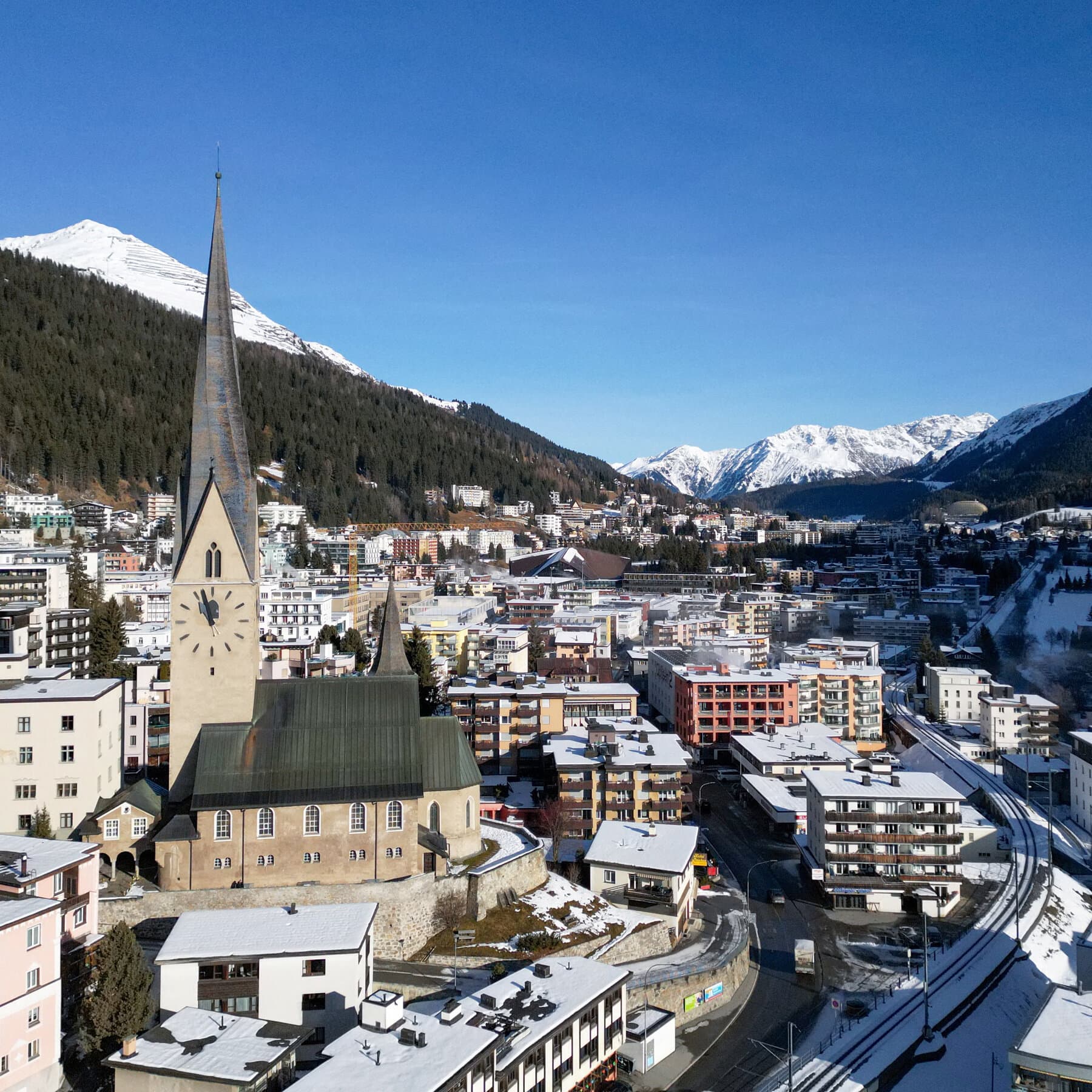 A satirical photorealistic news image showing a crowded snowy tarmac in the Swiss Alps jam-packed with hundreds of luxury private jets. In the foreground, a billionaire in a thick parka is giving a thumbs up while holding a cardboard sign that says 'SAVE THE EARTH.' The sky is filled with gray smog.