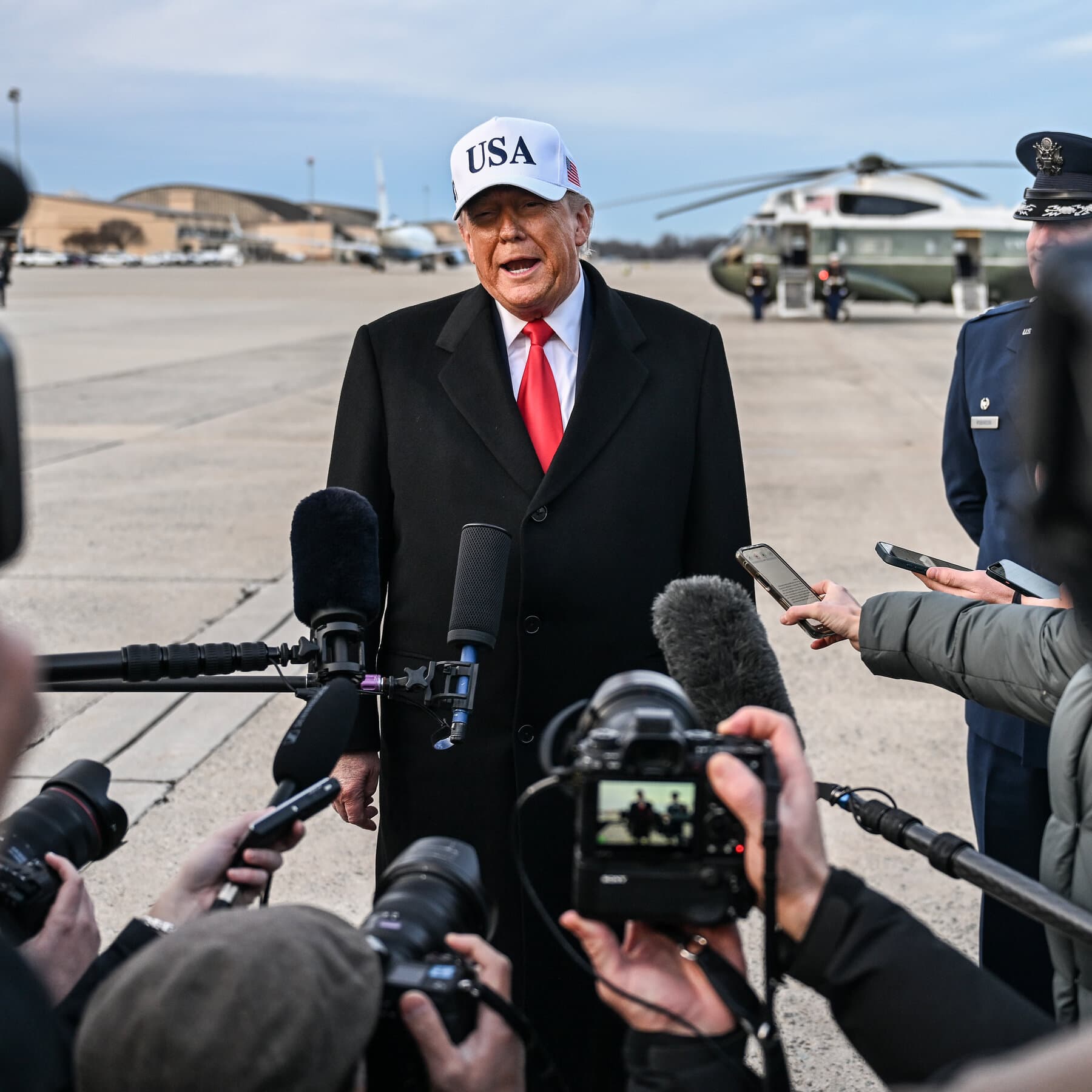 A satirical editorial illustration of a crumbling golden skyscraper shaped like a dollar sign, with a spray-tanned figure in an oversized suit standing on the roof throwing paper money into a dark storm cloud. Below, a group of people wearing 'Red' and 'Blue' jerseys fight over a single copper coin in a pothole-filled street. The style is dark and gritty, reminiscent of Ralph Steadman's ink splatter work.
