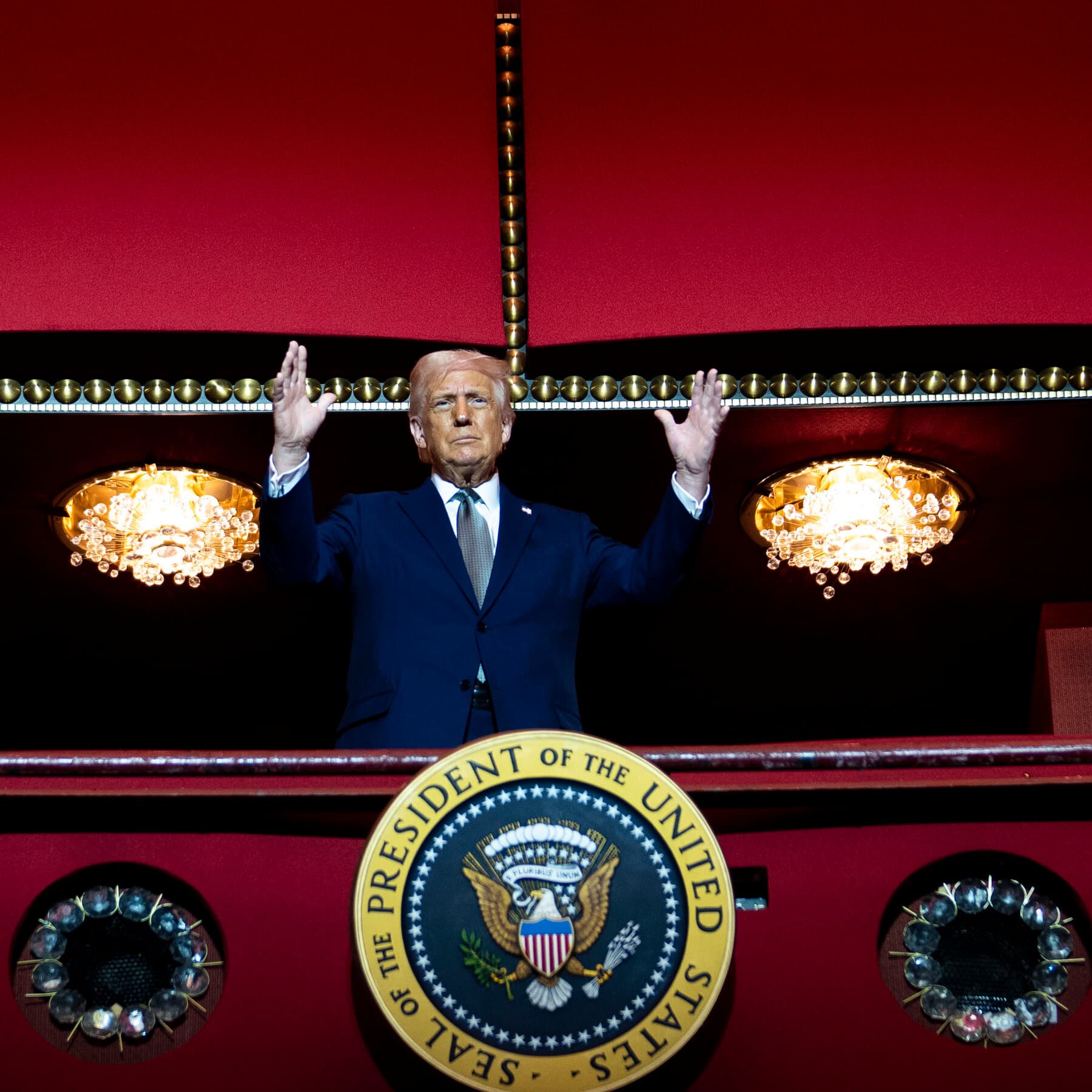 A cynical, tired journalist with graying hair sitting in a dark room illuminated by the glow of twenty flickering television screens, all showing the same distorted, orange-tinted face. The journalist is holding a glass of scotch and staring at a blank typewriter, while outside the window, a chaotic parade of people in red and blue hats are fighting over a giant jigsaw puzzle that has no actual pieces.