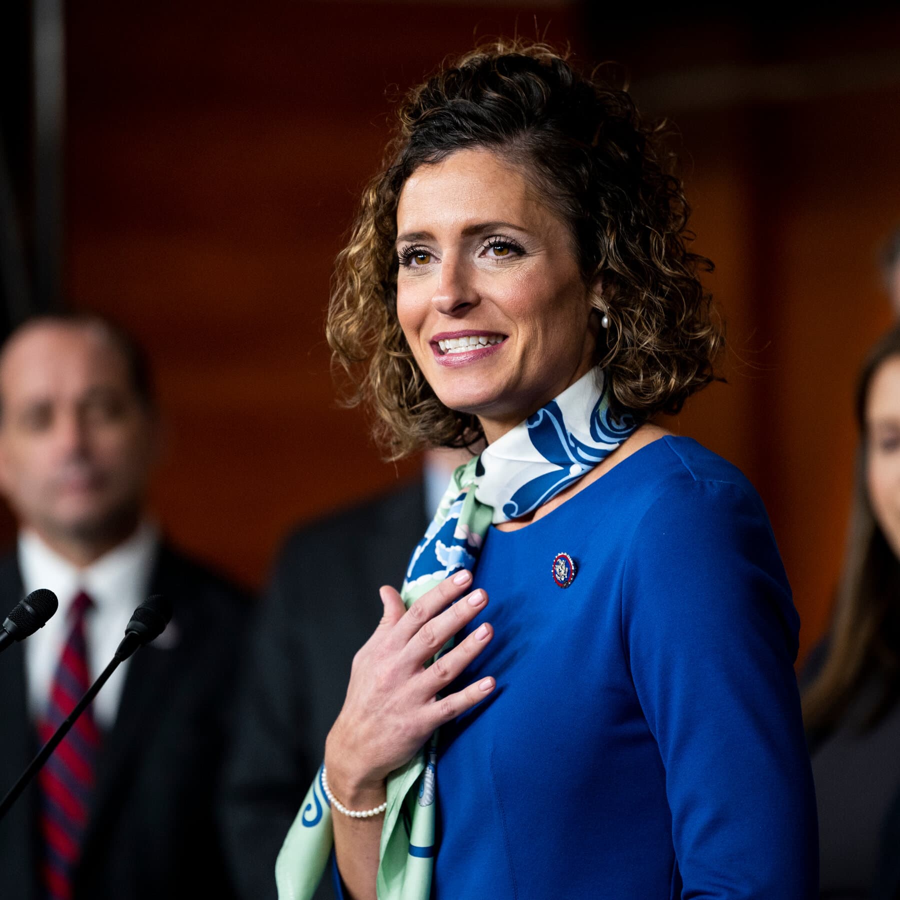 A satirical political cartoon style image depicting a Louisiana swamp at dusk. In the center, two elephants are fighting in the mud. One elephant looks tired and beleaguered, wearing a Senate pin. The other elephant is shiny, aggressive, and being directed by a large, looming, orange-tinted shadow in the background. Cypress trees draped in moss surround them, but the moss looks like tangled ticker tape. The atmosphere is gloomy, humid, and oppressive.