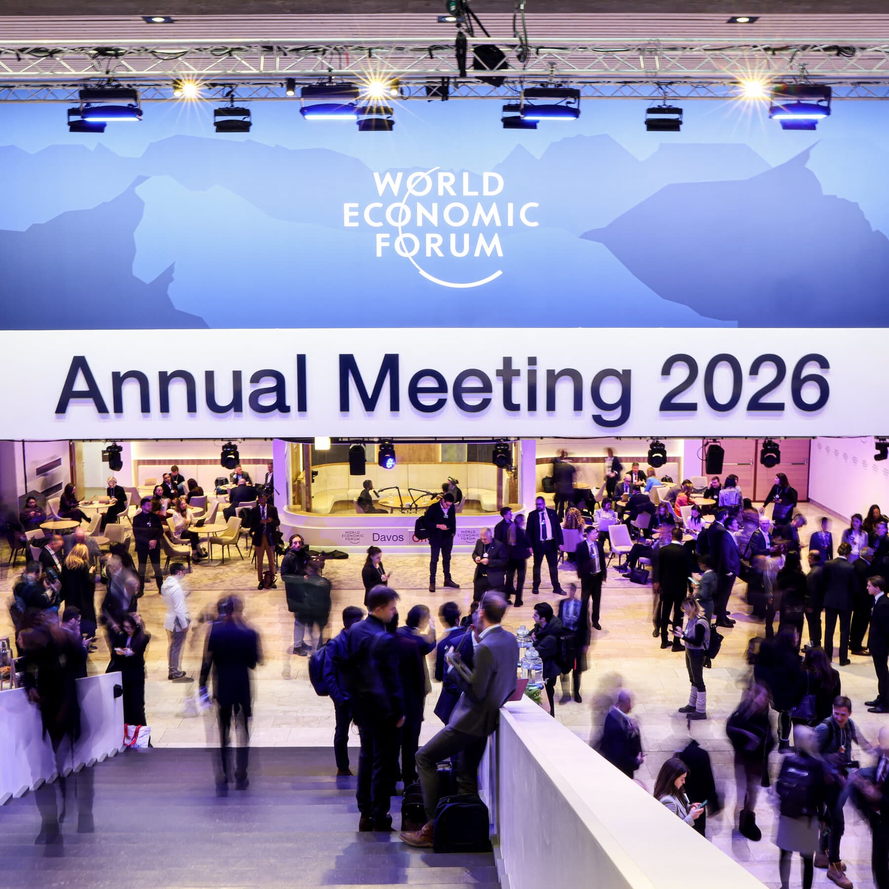 A satirical photorealistic image of the World Economic Forum in Davos. In a snowy, luxurious conference center, a massive, glowing, ominous computer server rack towers over the room, wearing a tuxedo. In the foreground, Donald Trump and Mark Zuckerberg are high-fiving while drinking champagne. In the background, sad-looking diplomats and UN peacekeepers are being physically swept out the door with brooms by robot security guards.