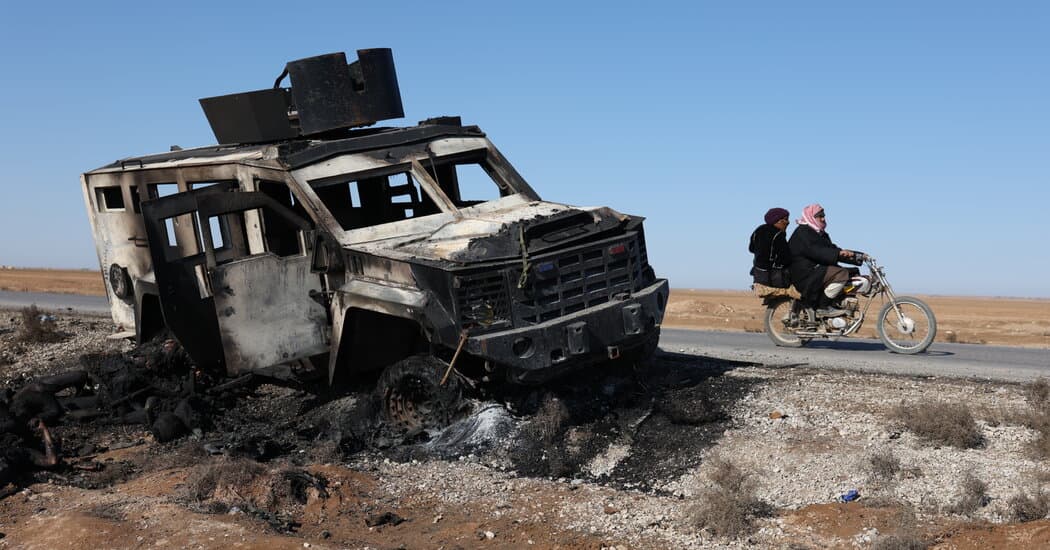 A wide-angle, cinematic shot of a tattered, dusty Kurdish flag lying half-buried in the sand of a desolate Syrian desert. In the far distance, a convoy of American military vehicles is seen driving away toward the horizon, leaving behind a trail of thick, dark smoke. The lighting is a harsh, cynical sunset, casting long, mocking shadows across a landscape of ruins. No people are visible, only the discarded remnants of a broken alliance.