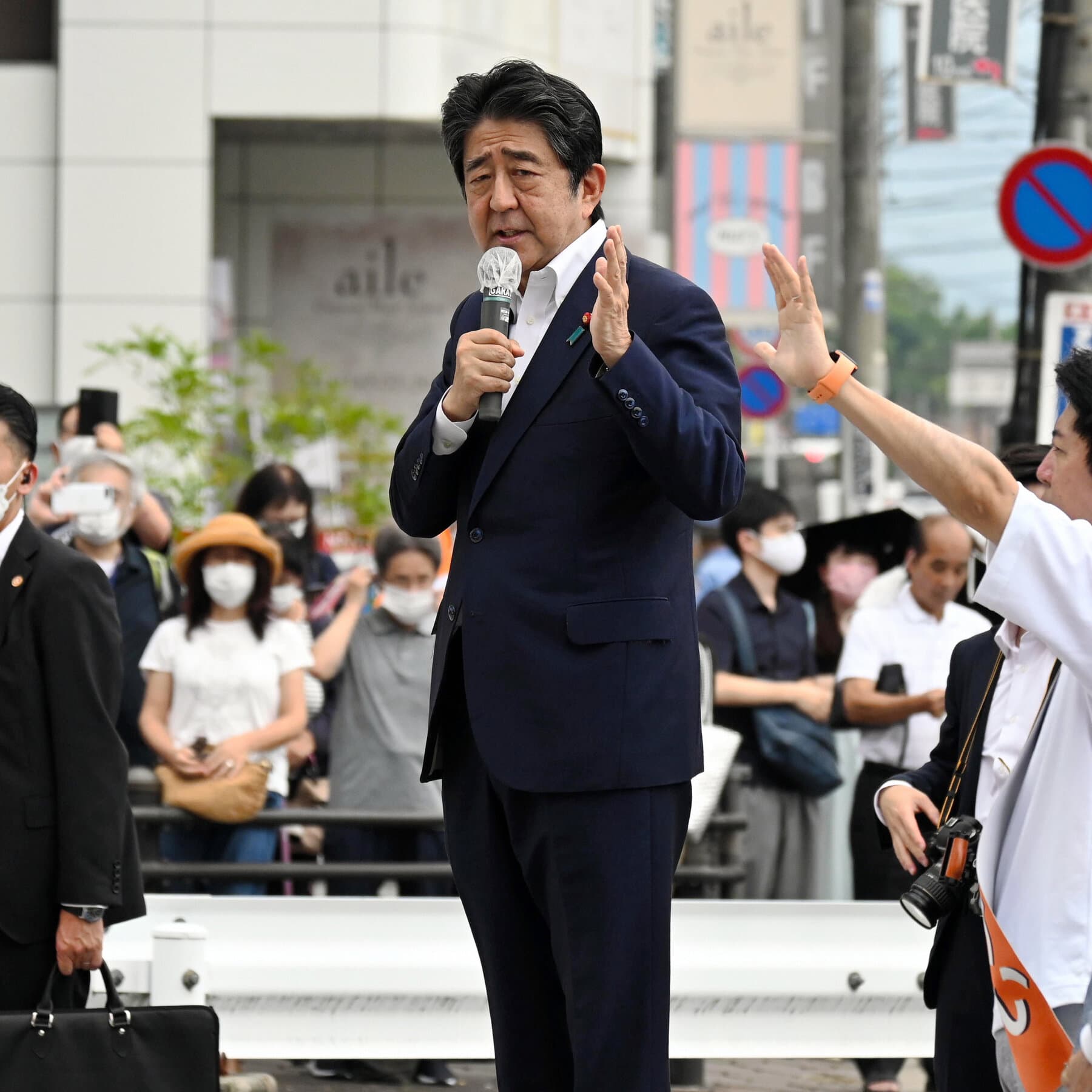 A cynical, high-contrast editorial illustration of a gavel shaped like a piece of rusted pipe, resting on a stack of yen notes and religious pamphlets. In the background, a silhouette of a faceless politician stands before a group of bowing followers, all set against a stark, industrial grey background in a gritty, satirical style.