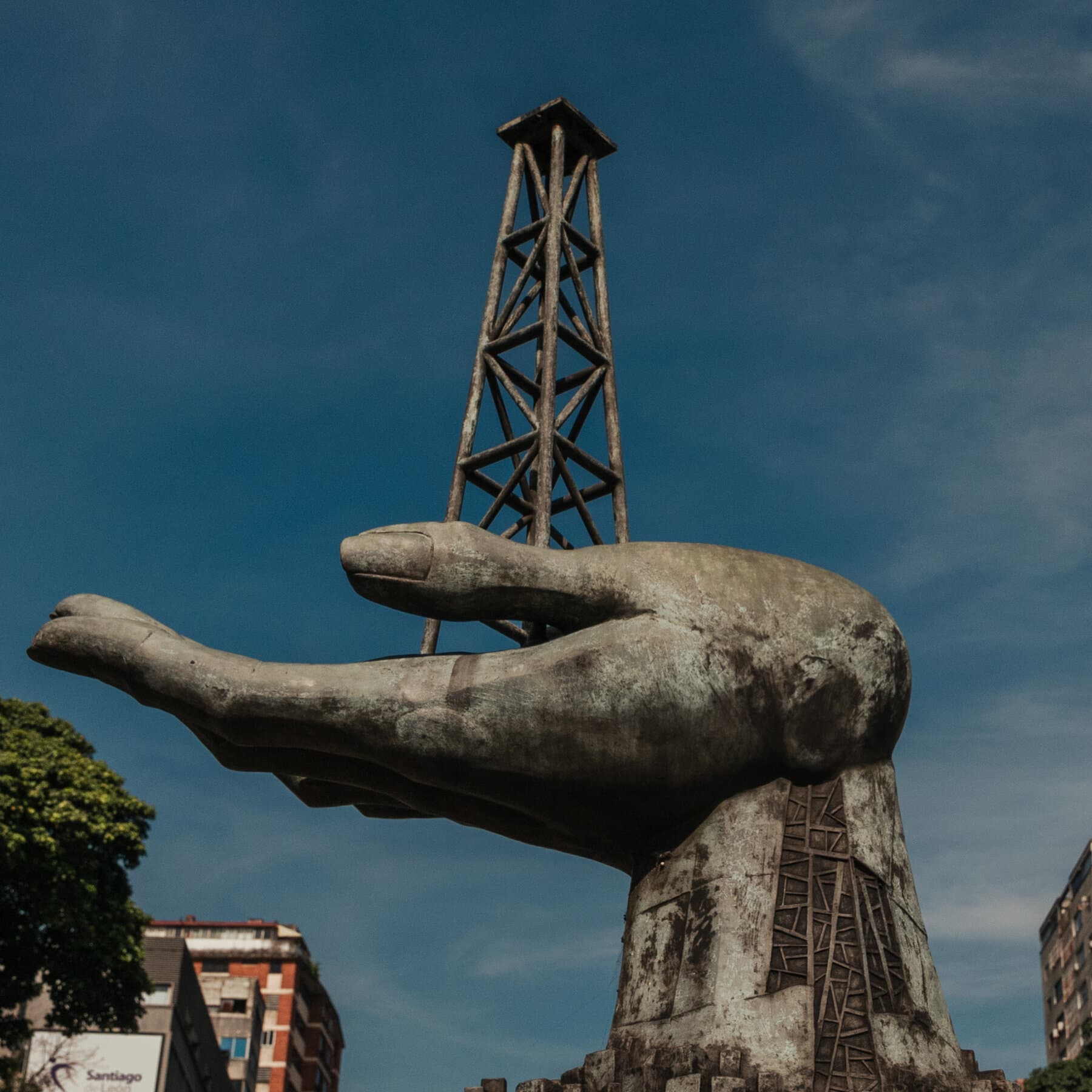 A satirical news photo of Donald Trump standing at a podium in the White House briefing room, pointing a laser pointer at a map of Venezuela where the entire country has been replaced by a giant logo of a gas can. He looks serious and patriotic.